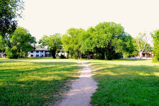 A well-worn field east of Airport Blvd adjacent to an apartment complex, industrial park, and a church.